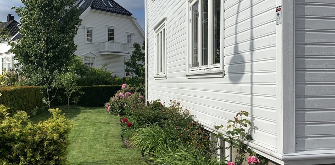 Leiligheten sett utenfra. 1. Etasje med to store vindu og underetasje som skimtes.