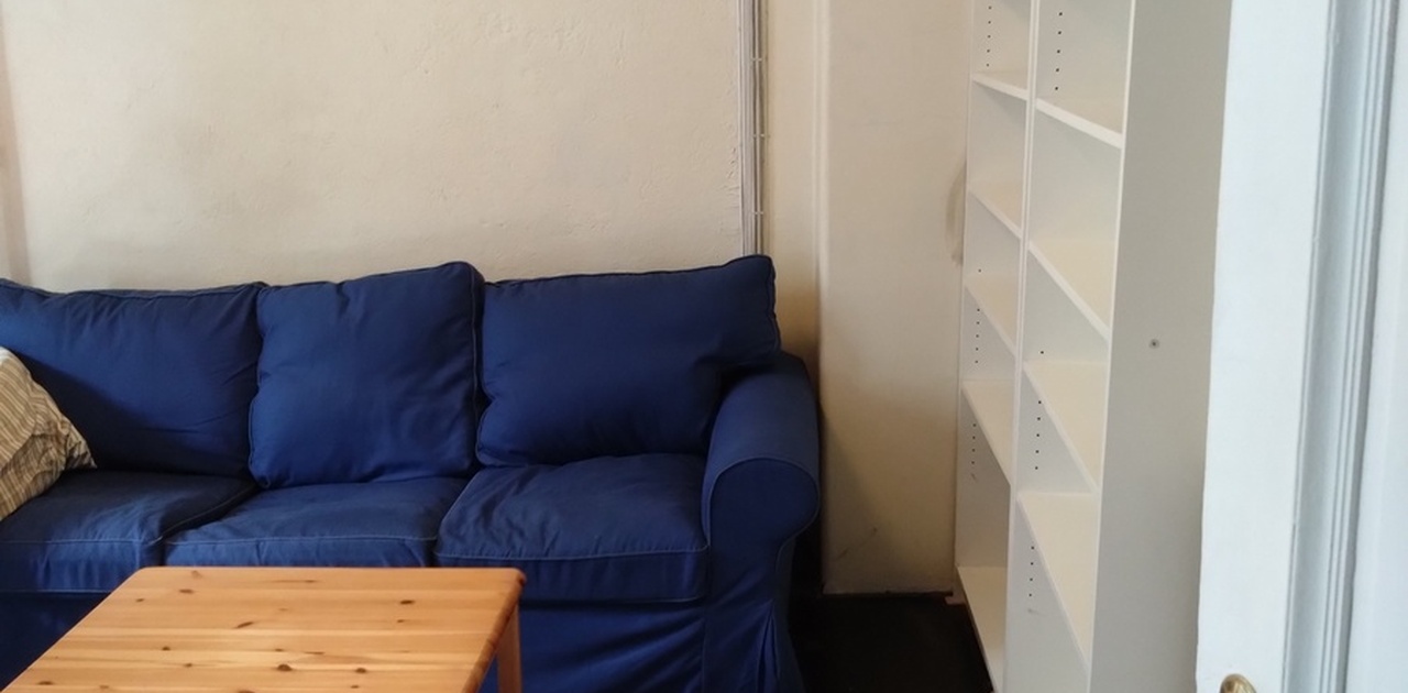 Inngang til hybel. Viser bokhyller, bord og sofa.