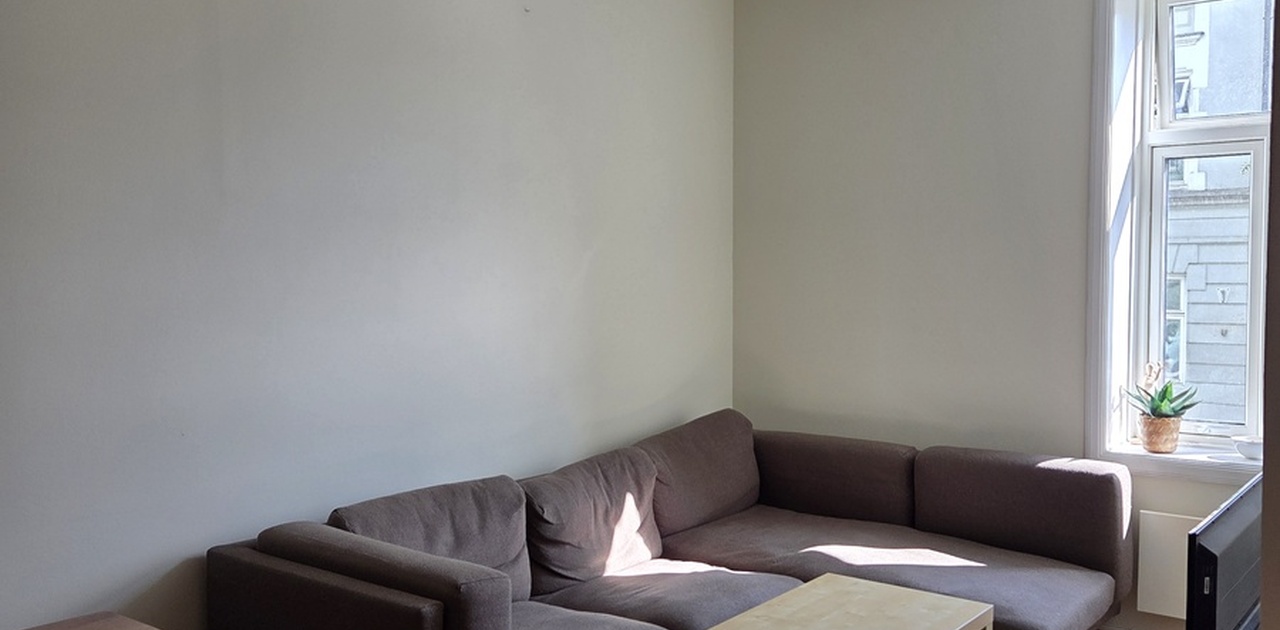 Lys og hyggelig stue med stor hjørnesofa, sofabord og stort vindu som slipper inn dagslys.