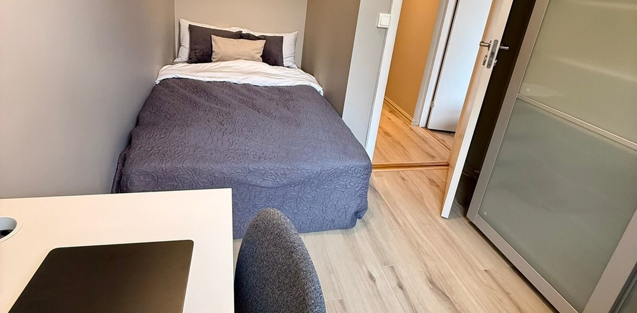 Soverom med seng, stort skap, skrivebord og stol.