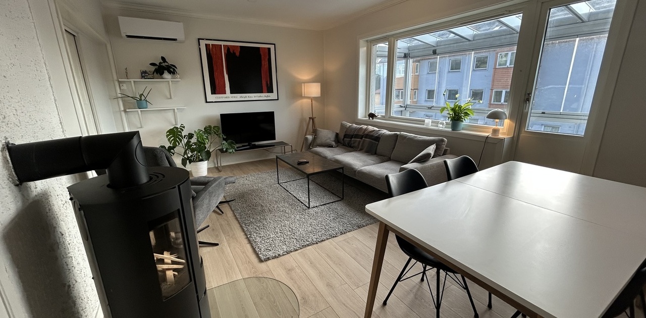 Stue1: Stor stue med sofa, lenestol, TV og spisebord. Dør til innglasset balkong ved siden av sofaen.