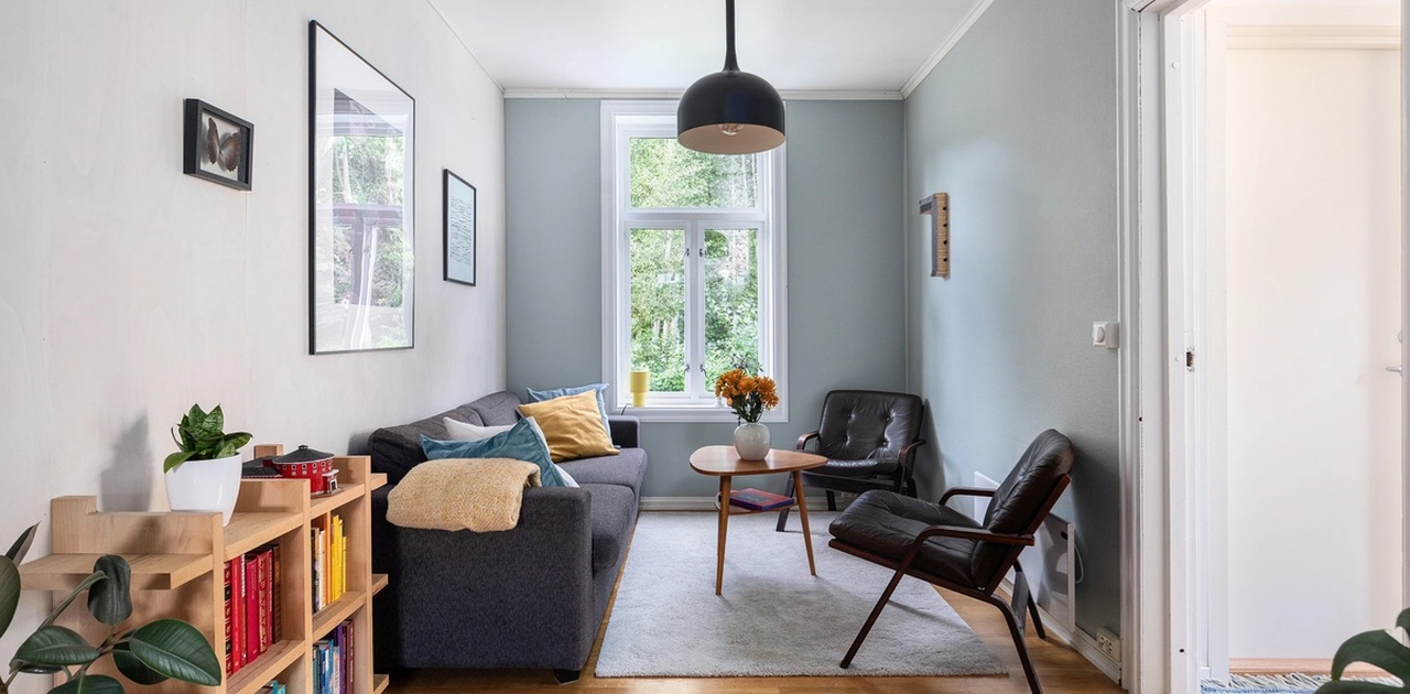 Romslig stue, med store vindusflater som er delvis adskilt fra kjøkken.