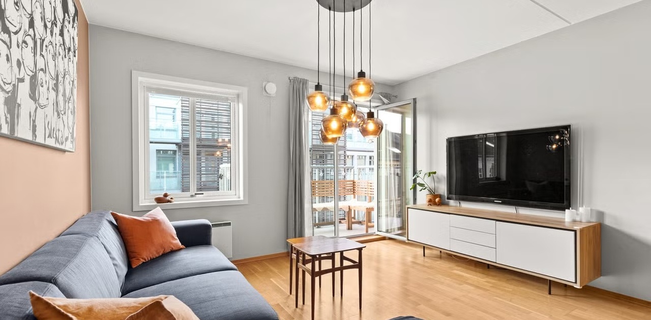 Stue med sofa og tv, dør til balkong. OBS: Møblene på bilde er utdaterte.