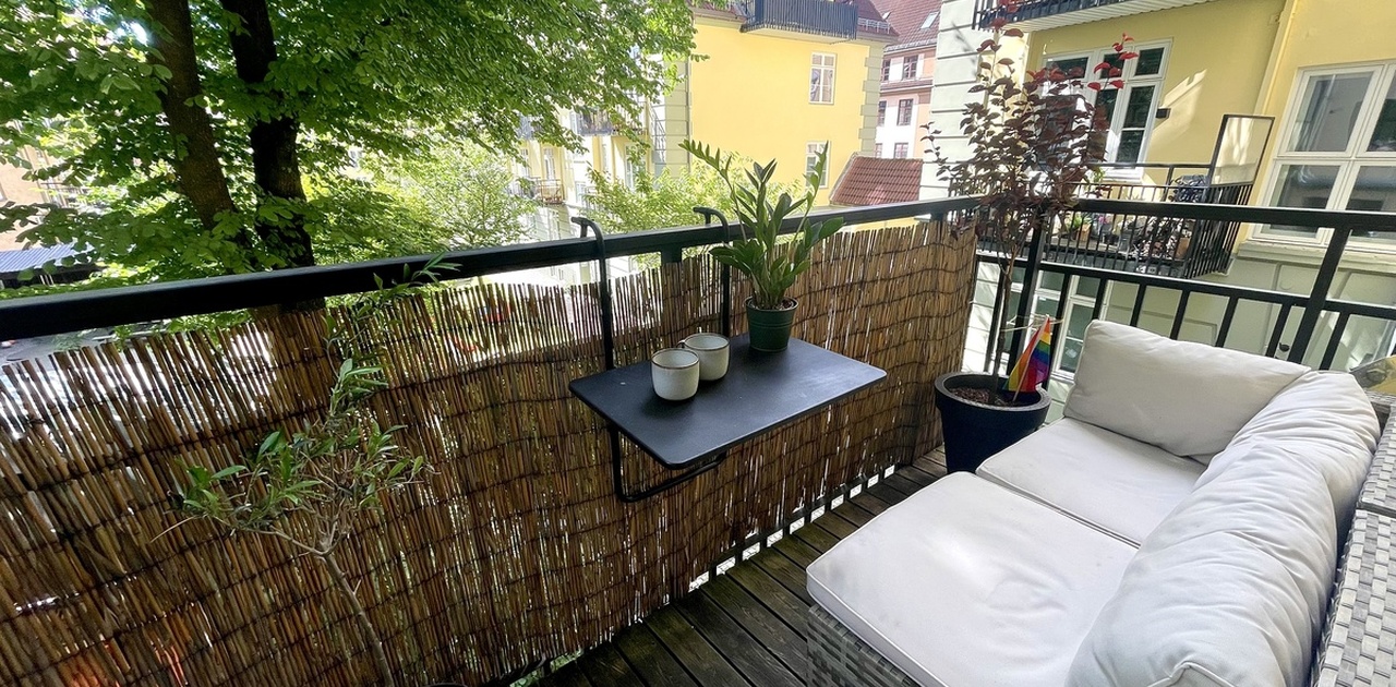 Sydvendt balkong med utesofa mot den frodige bakgården.