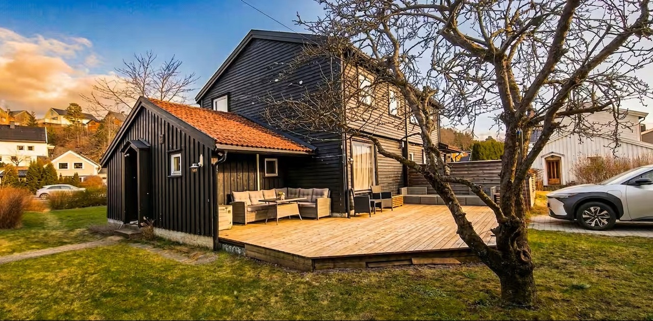 Autentisk svart norsk trehus med stor terrasse og loungemøbler — lyst og innbydende