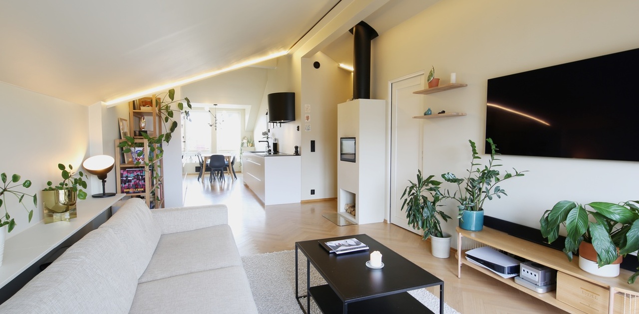 Stue, kjøkken og spisestue i åpen løsning, med peis, moderne hvitevarer og masse lys, uten gjengangere.