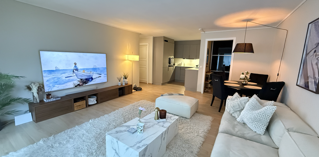 Romslig og lys stue med åpen løsning mot spiseplass og kjøkken, som skaper en sosial og luftig atmosfære. Stuen er fullt møblert med stor sofa, spisebord og stor TV, og har direkte utgang til terrasse og hage.
