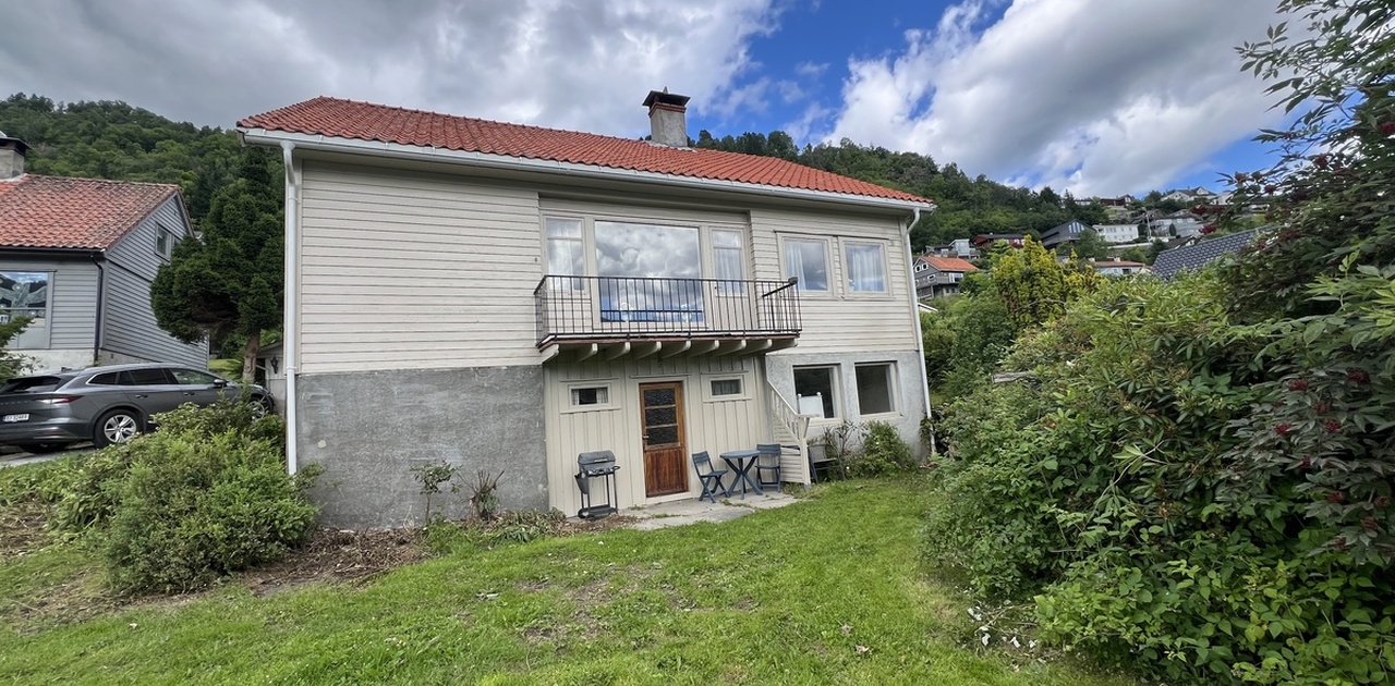 Huset frå framsida. Flat hage og dobbel garasje til venstre.