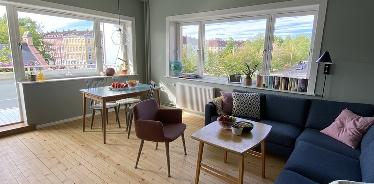Romslig stue med hjørnesofa, tv og spisebord. Vindu på to vegger gir mye lys