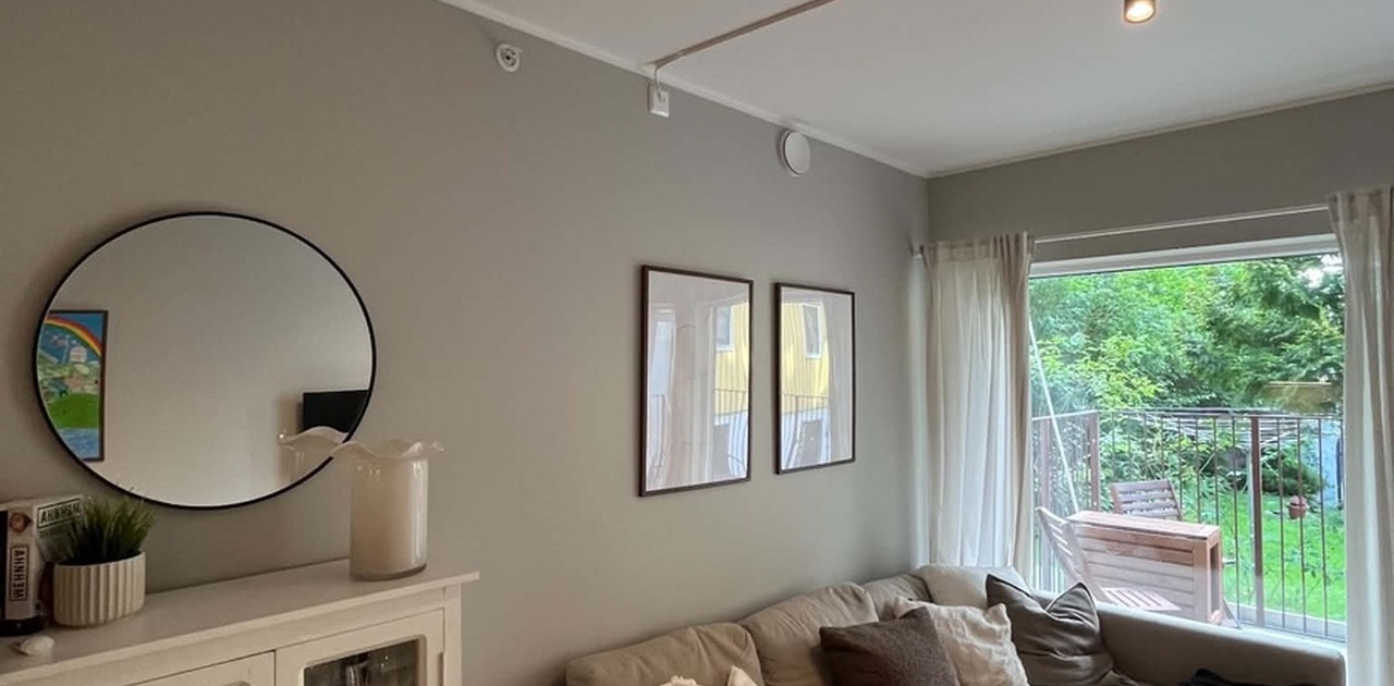 Stuen har en beige hjørnesofa og et vitrineskap, med direkte utgang til en balkong med grønne omgivelser.