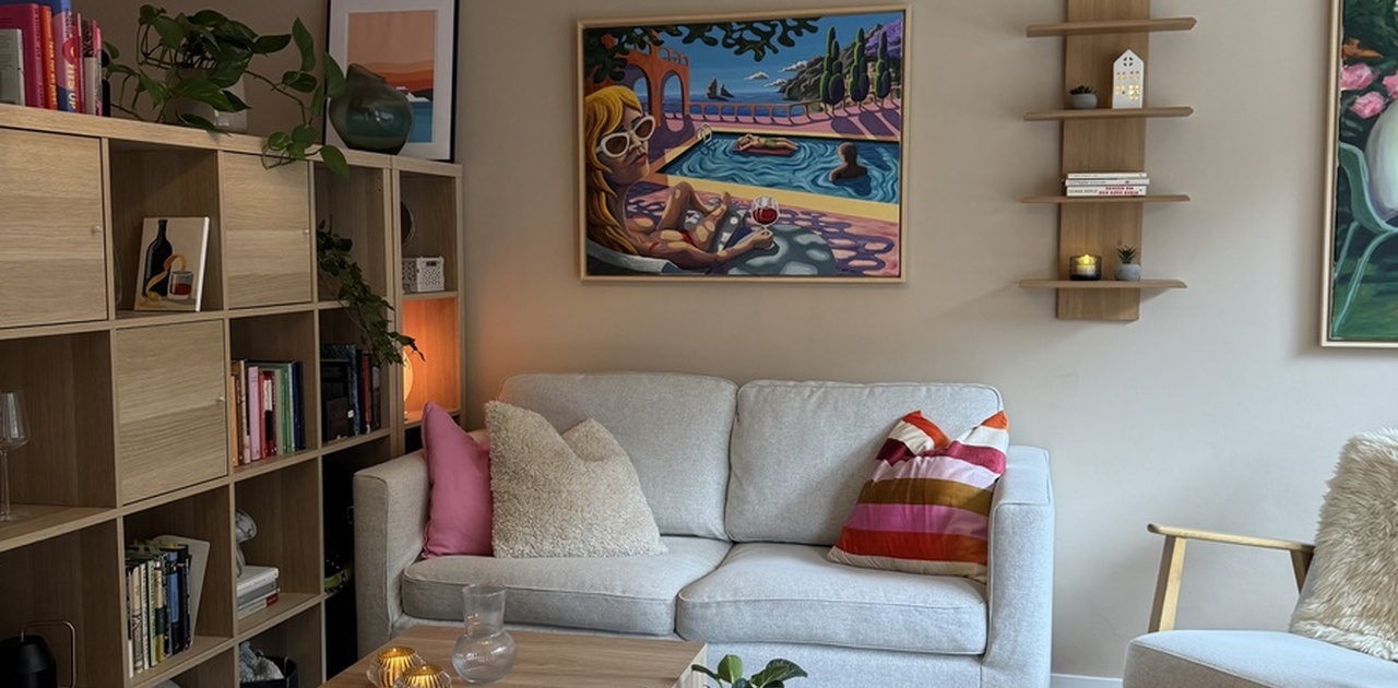 Stuen har en hyggelig sittekrok med en lys toseters sofa, lave trebord og fargerik kunst på den beige veggen.