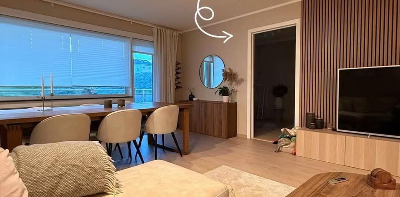 Stuen rommer en trivelig sittegruppe, langbord ved vinduet og en moderne spilevegg ved TV-kroken.