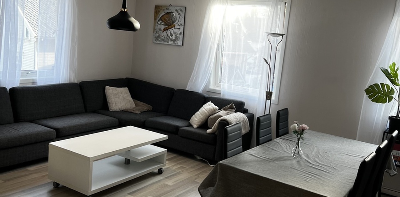 Stuen er innredet med en romslig mørk hjørnesofa, hvitt salongbord og et spisebord plassert ved vindusflatene.
