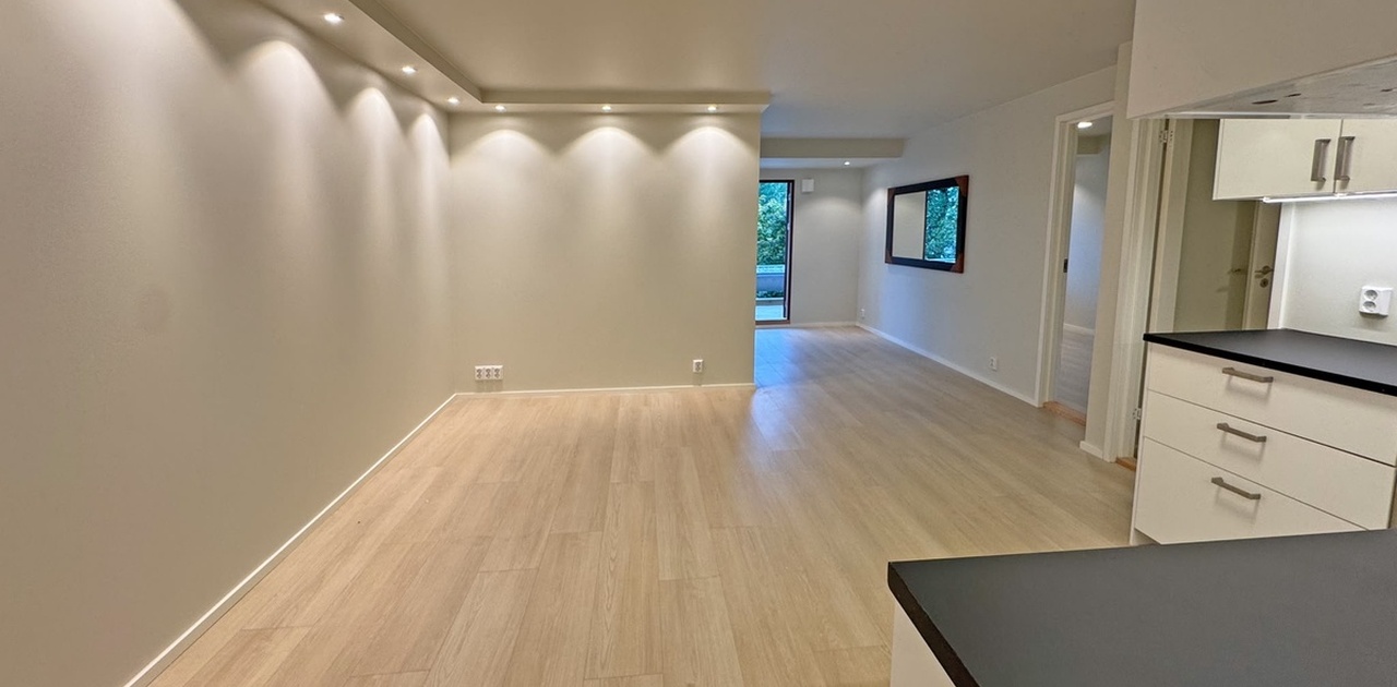 Innfelt spottbelysning i taket kaster stemningsfullt lys over det lyse gulvet i den åpne stueløsningen.