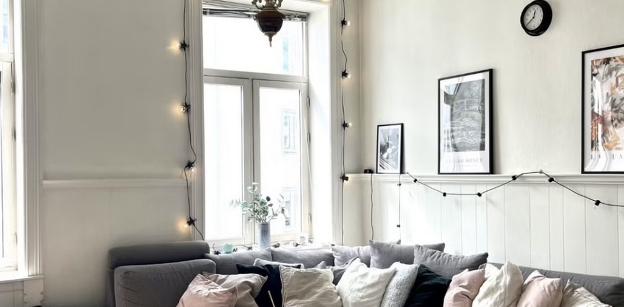 Stuen preges av klassisk stukkatur og takrosett, kombinert med en stor hjørnesofa og lysgivende vinduer.