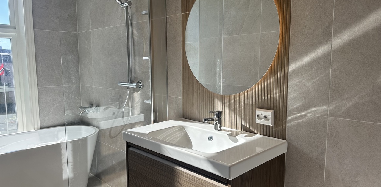 Badet har en stilren servantinnredning med et bakbelyst runde speil montert på spiler, samt et frittstående badekar og dusjsone med regndusj.