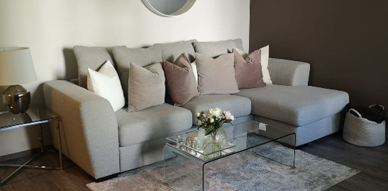 Stuen har en grå sjesselongsofa kombinert med et stilrent sofabord i glass og et rundt speil på veggen.