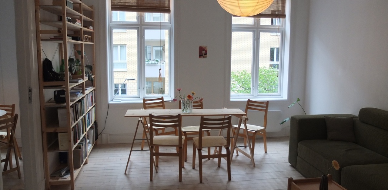 Stue med spisebord, sofa og peis. Originale tregulv og klassisk stukkatur. Noe av møblene (blant annet spisebordet) er litt midlertidig og kan endre seg.