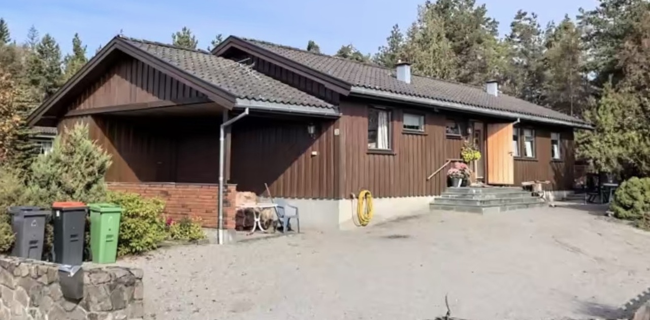Eneboligen har mørk trekledning, romslig gruset gårdsplass med biloppstillingsplass og skjermende steinmur i naturskjønne omgivelser.
