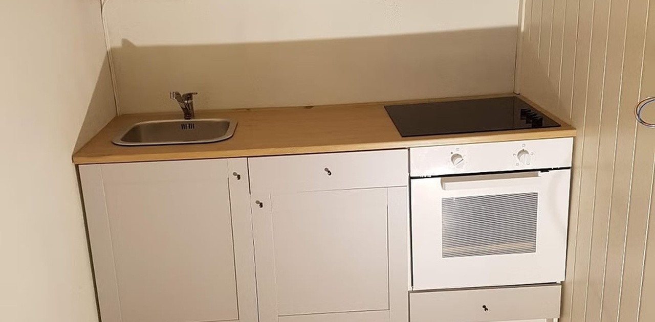 Det kompakte kjøkkenet har grå skapfronter, lys benkeplate og mørkegrå fliser på gulvet.