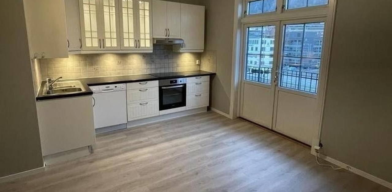 Kjøkkenet har hvit profilinnredning med integrerte hvitevarer, benkebelysning og en dobbel glassdør ut.