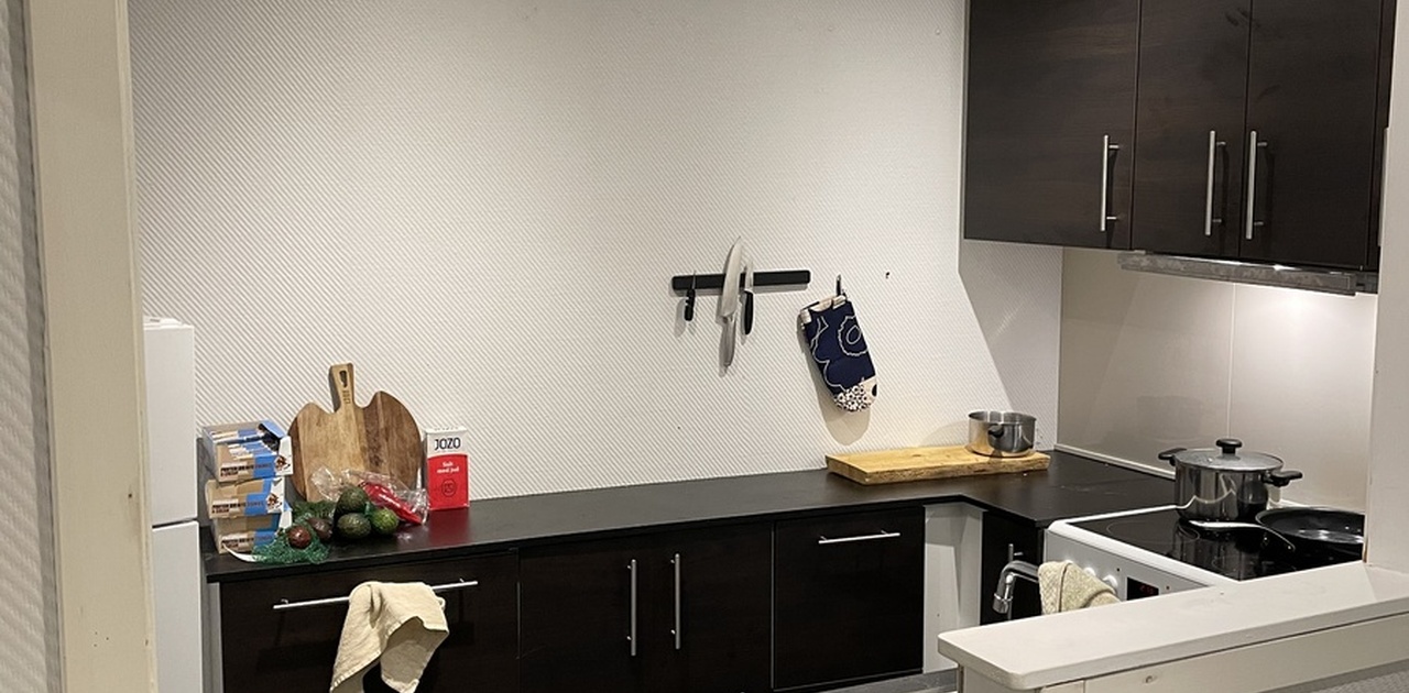 Kjøkkenkroken har mørke frontflater, mørkt flislagt gulv og moderne takbjelker med downlights.