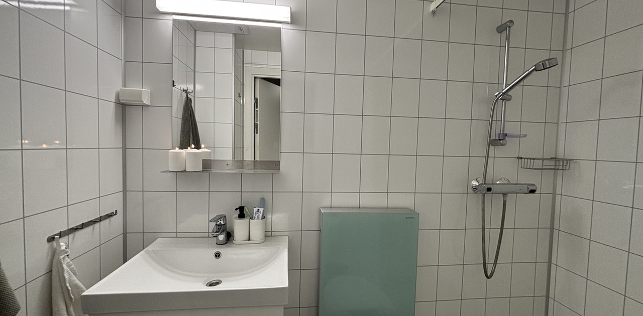 Badet er helfliset med hvite fliser og har et moderne toalett med mintgrønn glassmodul, servantmøbel og dusjsone.
