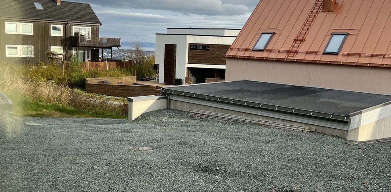 Utsikt over omkringliggende bebyggelse og gruslagt areal med glimt av sjøen i horisonten.