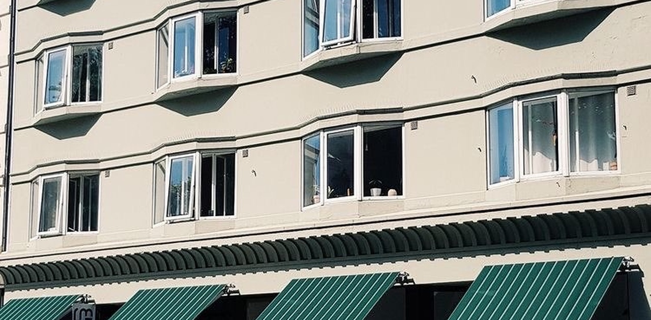 Bygårdens særegne fasade preges av utstikkende karnappvinduer og grønne markiser over butikklokalene på gateplan.