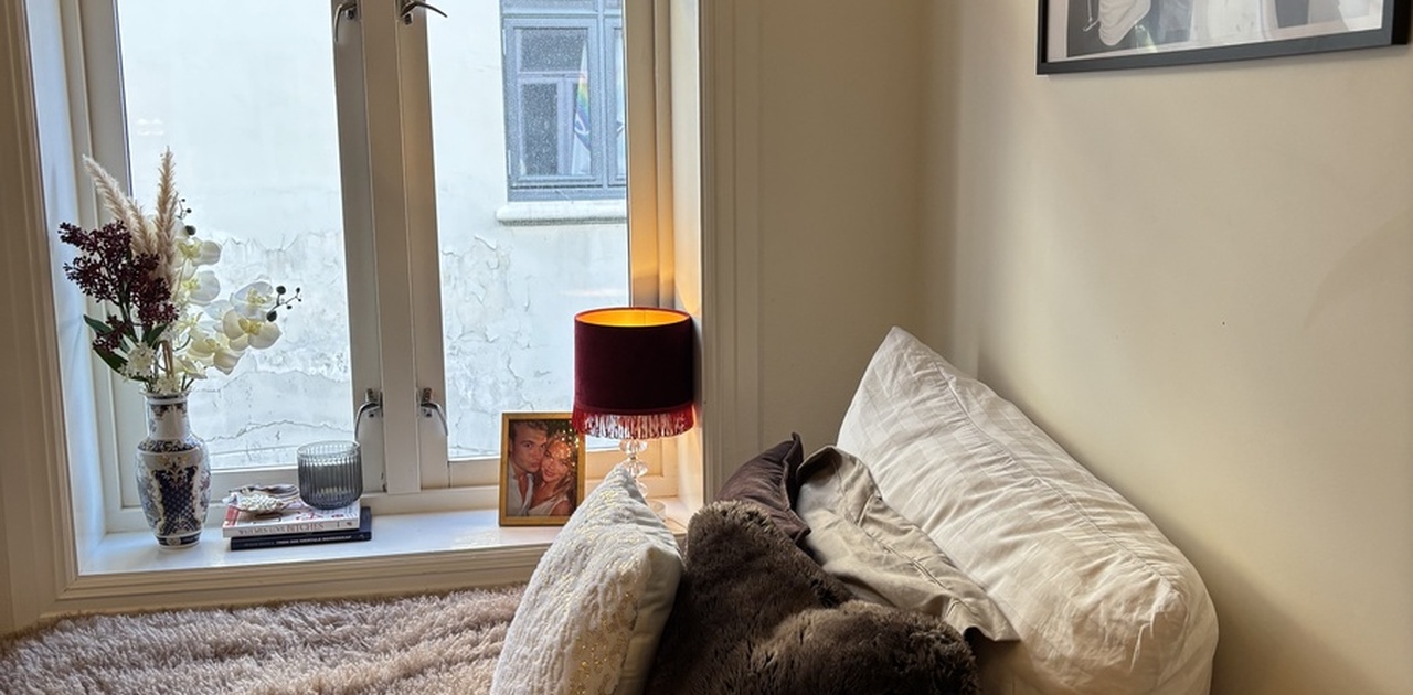 Soveromskroken er innredet med en seng inntil vinduet, dekorert med myke puter og stemningsfull belysning i vinduskarmen.