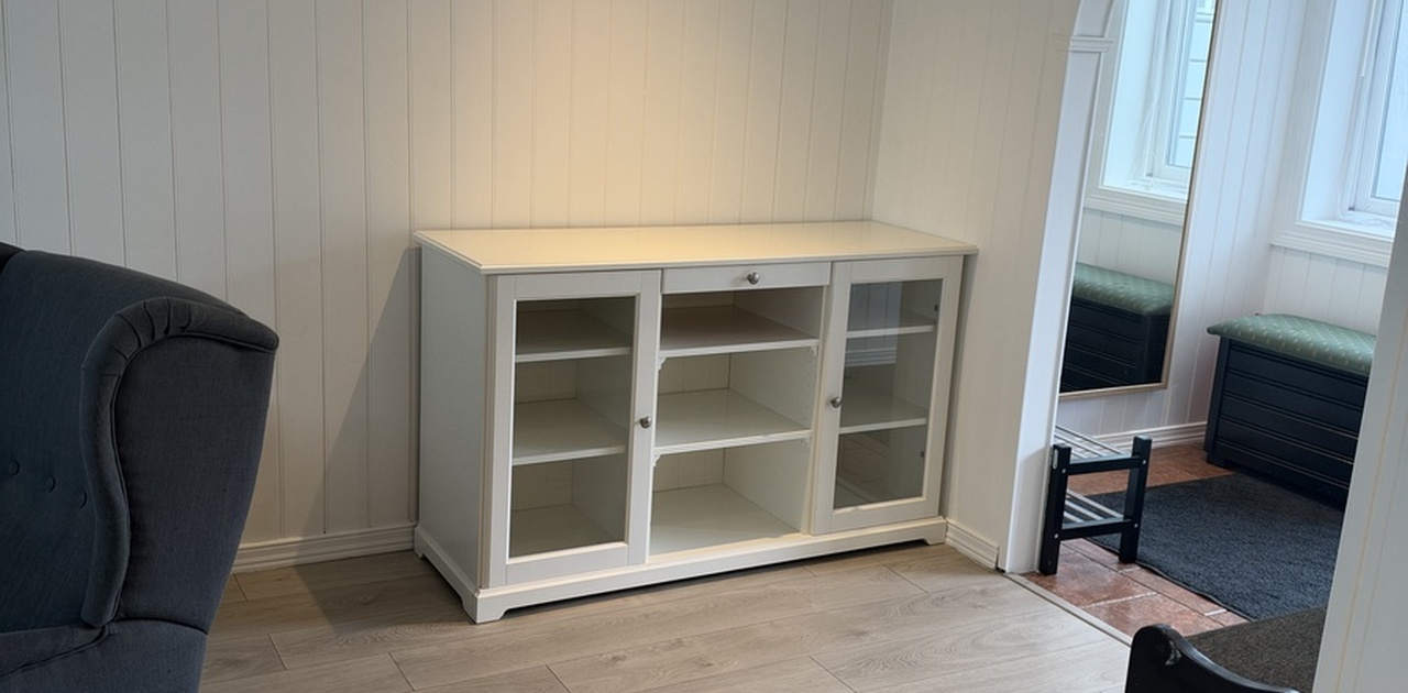 Stuen har lyst parkettmønstret gulv, hvitpanelte vegger med integrerte downlights og en buegang som fører inn til entréen.