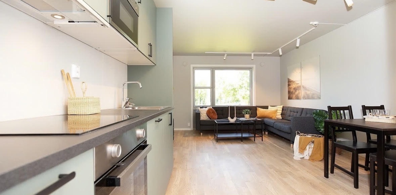 Moderne, fullt utstyrt åpen kjøkkenløsning med spisebord og stoler, mye naturlig lys og en koselig sofakrok – perfekt for matlaging, avslapning og sosialt samvær.
