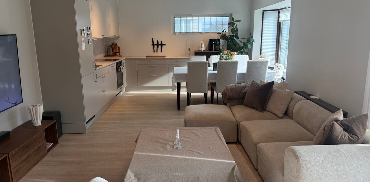 Den åpne stueløsningen kombinerer et stilrent kjøkken i duse toner med spiseplass og en romslig hjørnesofa.