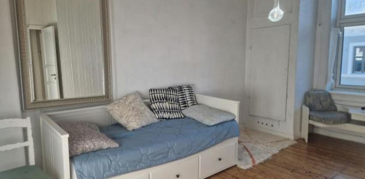 Soverommet er innredet med en hvit dagseng med oppbevaringsskuffer, et stort speil med profilert ramme og tregulv.