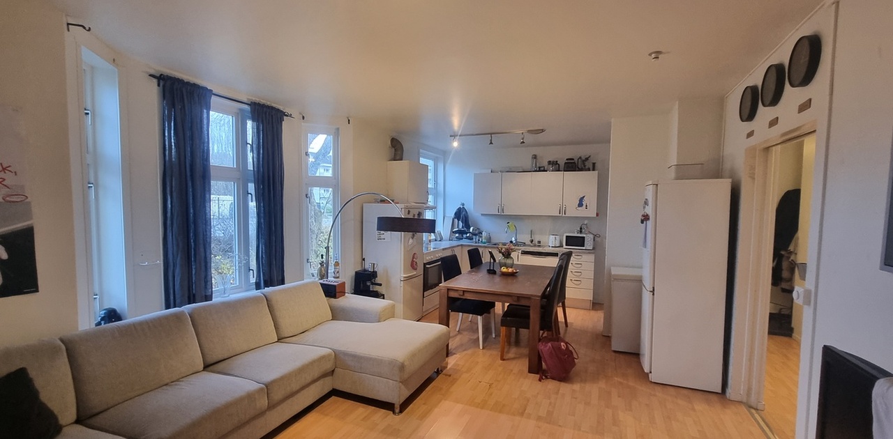 Den åpne stueløsningen har en stor, lys hjørnesofa og parkettgulv som strekker seg mot spiseplassen og kjøkkenet i bakgrunnen.