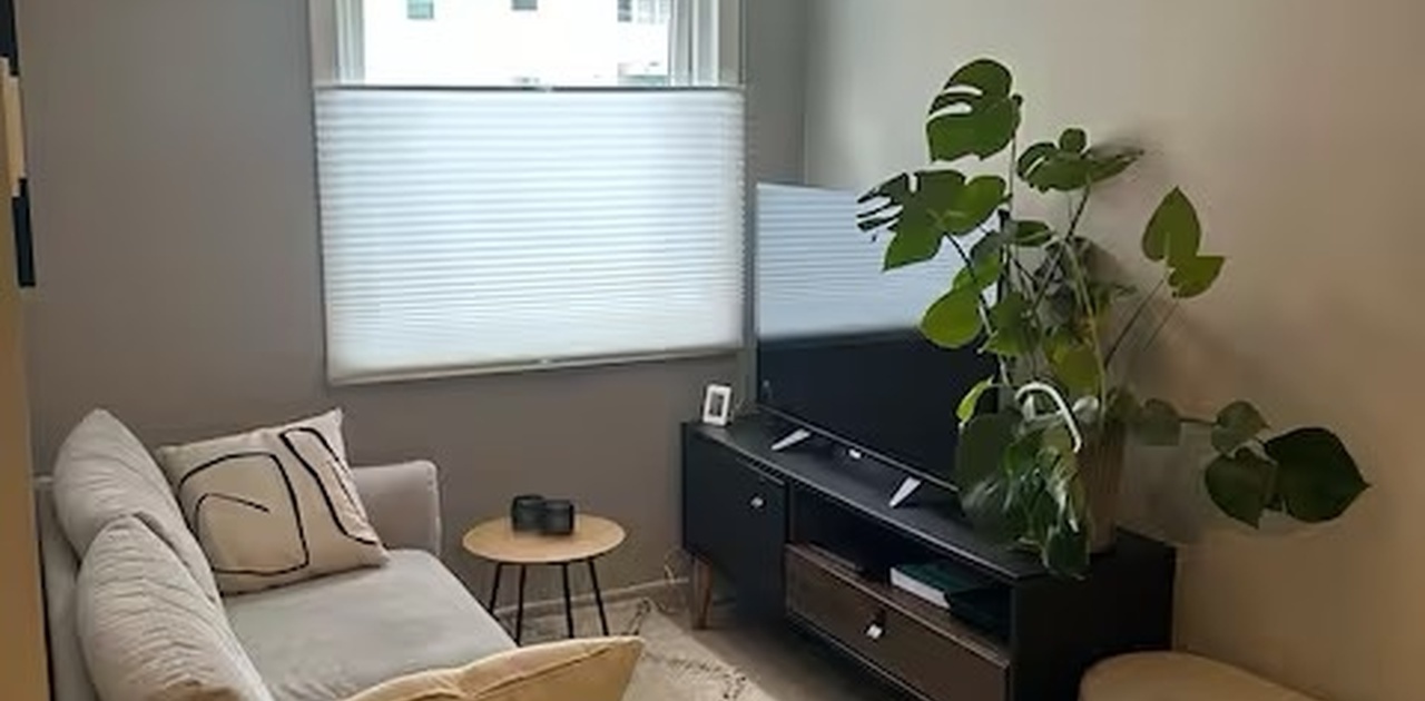 Stuen har en hyggelig TV-krok med lys sofa, mørk TV-benk og et mønstret gulvteppe under varm takbelysning.