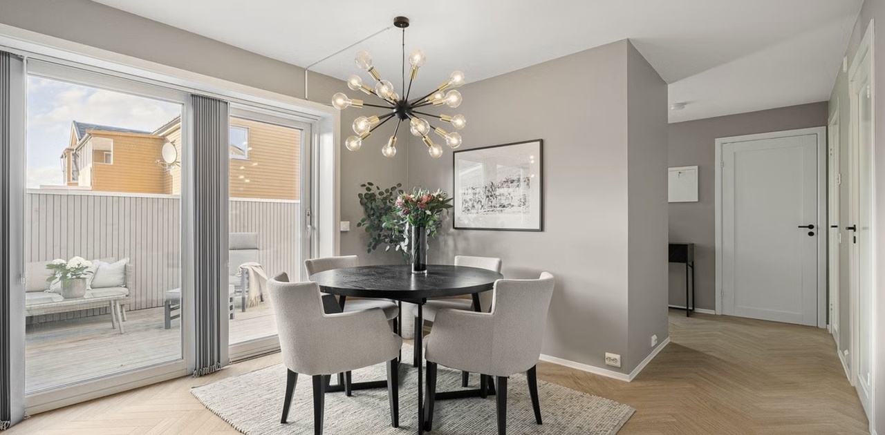 Spiseplassen har et mørkt rundt bord med stoppede stoler på elegant fiskebensparkett, placeret ved store skyvedører som fører ut til terrassen.