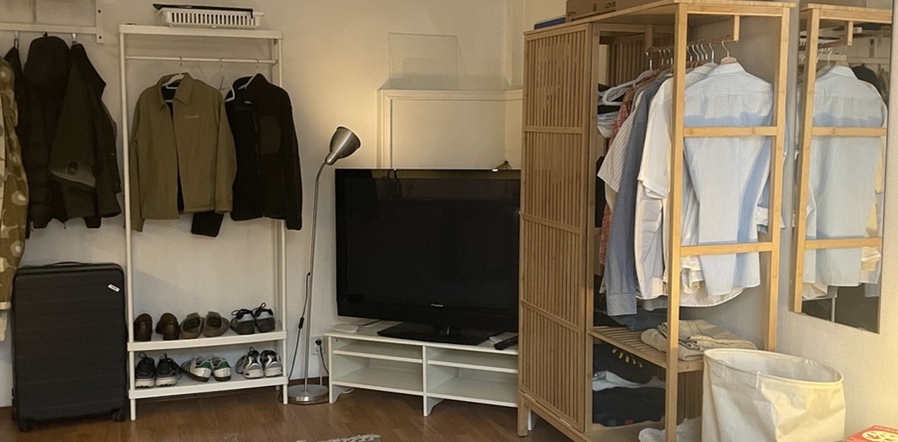 Oppholdsrommet kombinerer soveplass og TV-krok med åpne garderobeløsninger og parkett på gulvet.