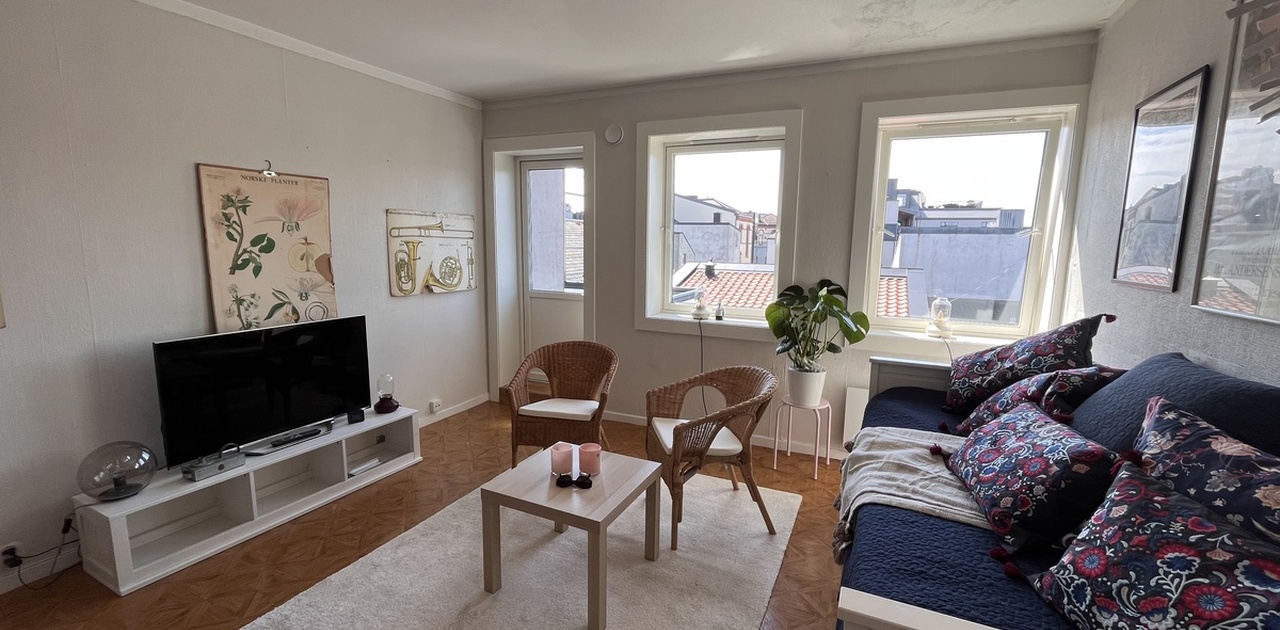 Dagseng, tv med chromecast, kurvstolee og bilder på veggene.