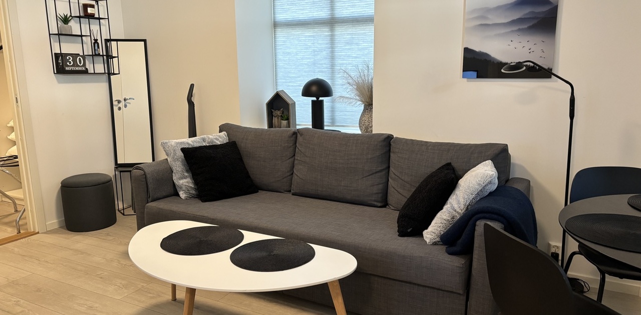 Stuen er innredet med en grå tre-seters sofa, et hvitt ovalt salongbord og lyst laminatgulv.