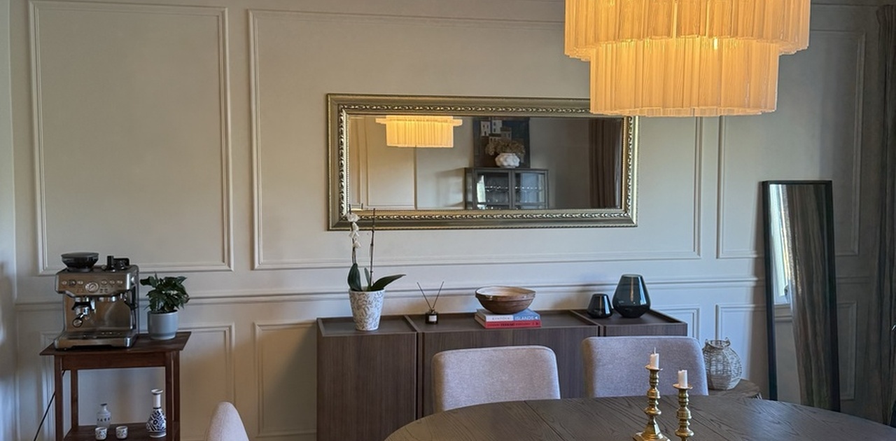 Spiseplassen er innredet med et rundt trebord og behagelige stoler under en stilig lysekrone og klassiske vegglister