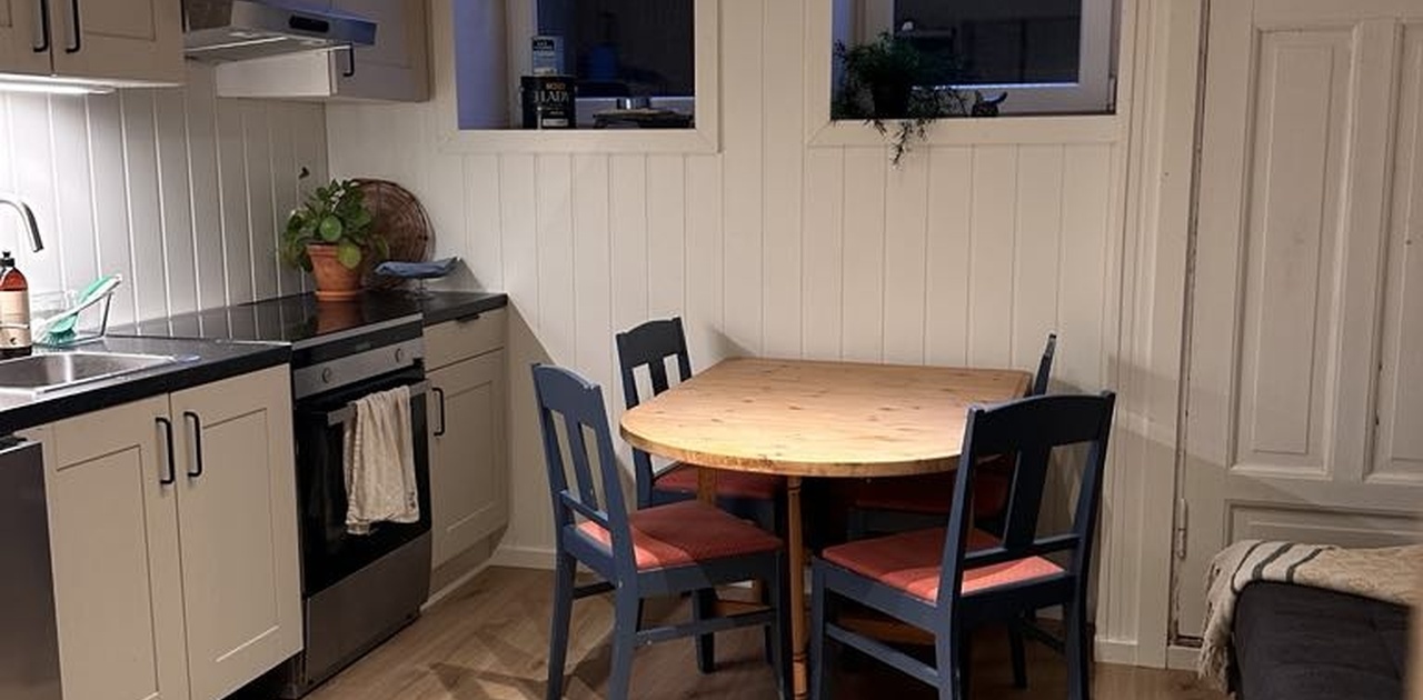 Kjøkkenet har grå innredning med integrerte hvitevarer og en hyggelig spiseplass plassert under to høye vinduer. Tv og oppholdsplass